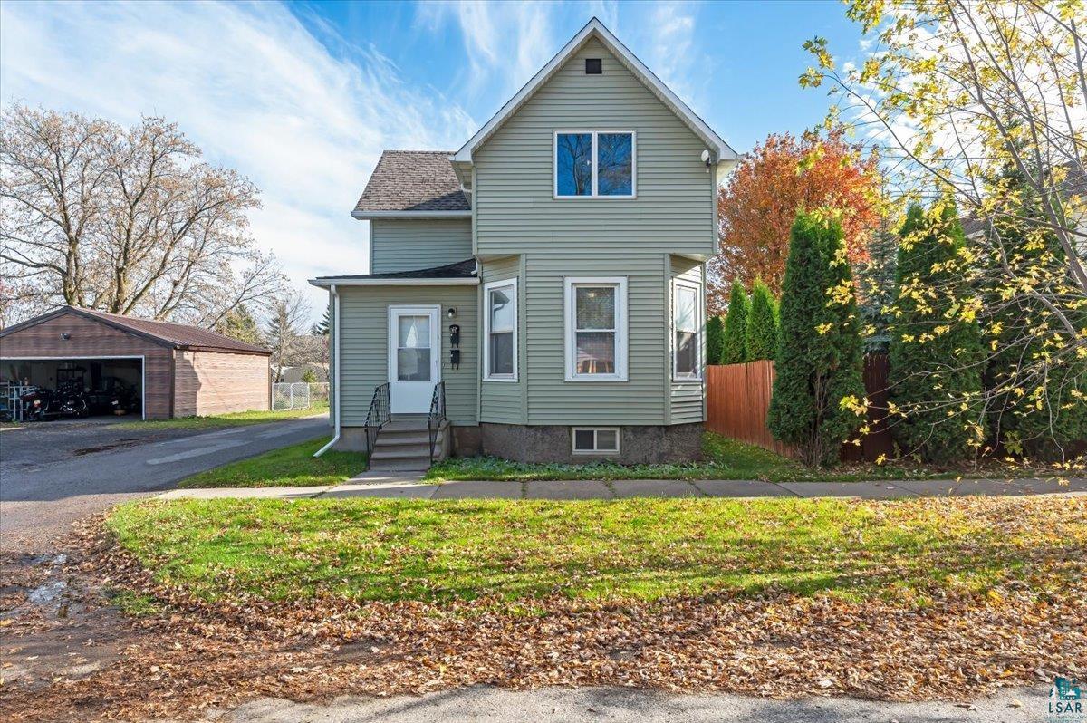 View of property featuring a garage, an outbuilding, and a front lawn