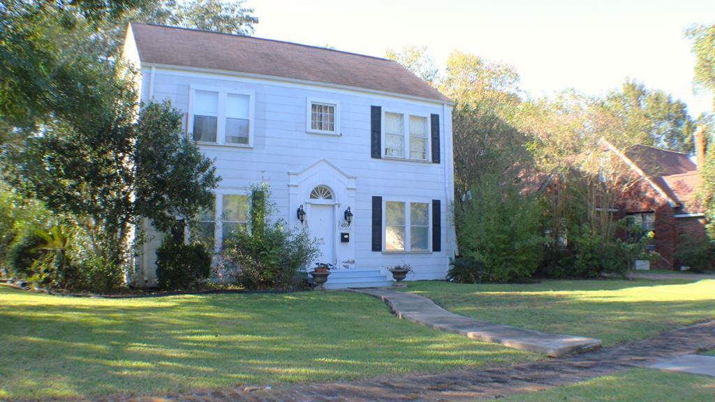 a brick house with a yard plants and big trees