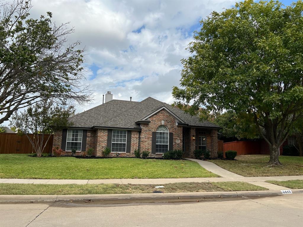 a brick house next to a yard with large trees