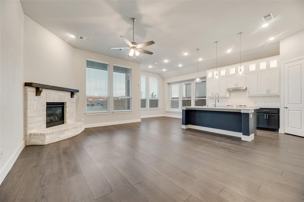 a view of an empty room with wooden floor and a kitchen