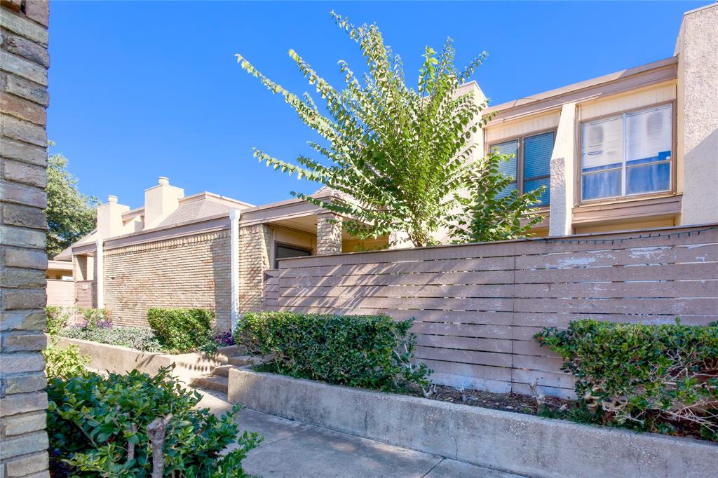 a view of a house with brick walls plants and large tree