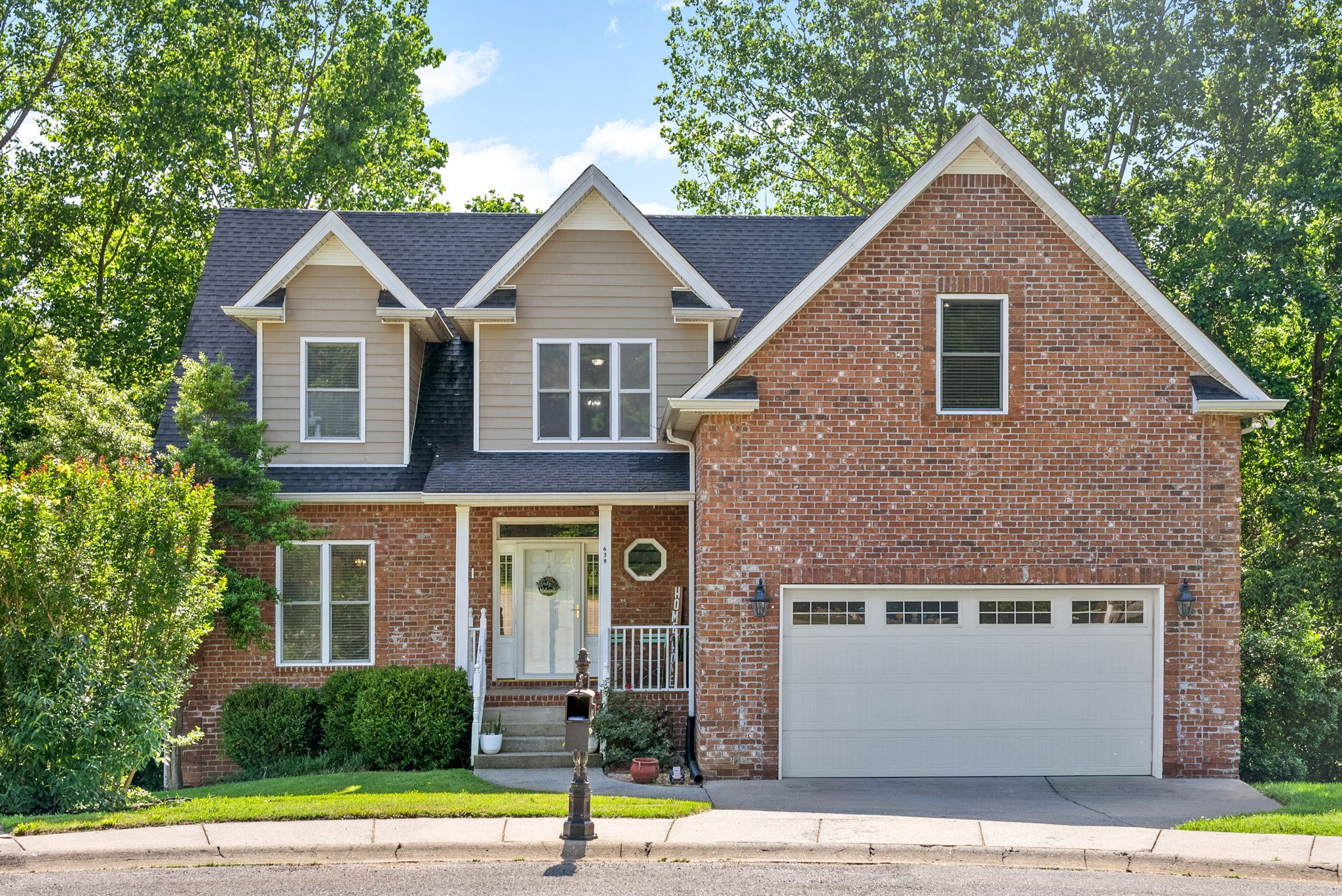 a view of a brick house with a yard plants and large tree