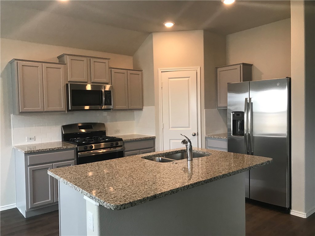 a kitchen with granite countertop a sink a counter top space cabinets and stainless steel appliances