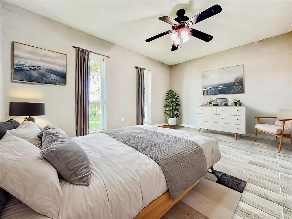 A bright, spacious bedroom with neutral walls, contemporary decor, and wood-look flooring is waiting for you. It features a ceiling fan, ample natural light from two windows, and modern furnishings.