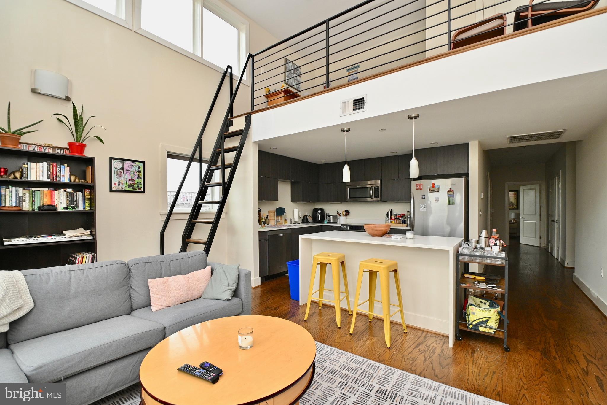 a living room with stainless steel appliances furniture a rug and a kitchen view