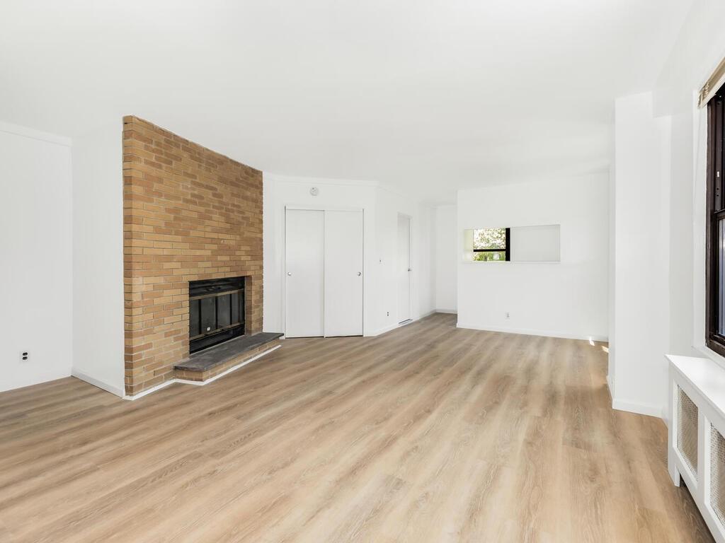 Unfurnished living room featuring brick wall, a brick fireplace, and light hardwood / wood-style flooring