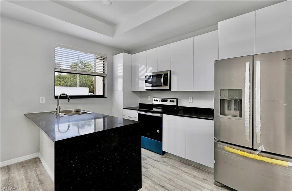 Kitchen featuring appliances with stainless steel finishes, sink, white cabinets, and light wood-type flooring