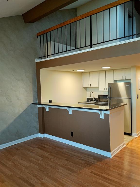 Kitchen featuring white cabinetry, a kitchen breakfast bar, kitchen peninsula, stainless steel fridge, and light hardwood / wood-style floors