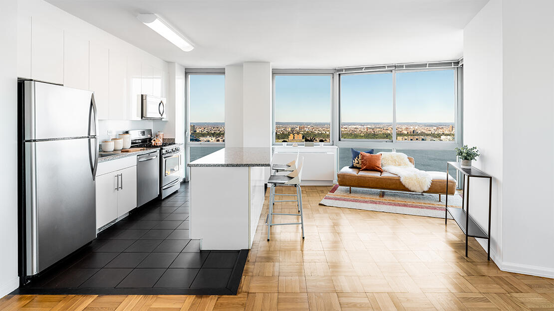 a living room with stainless steel appliances furniture a rug and a kitchen view