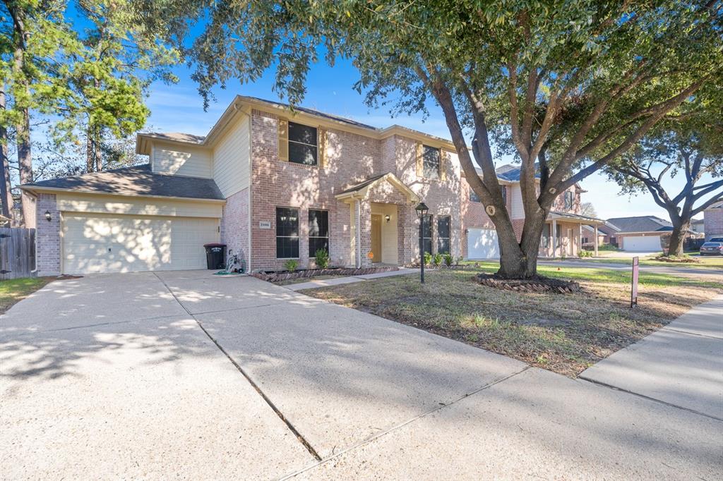 This photo shows a two-story brick home with an attached two-car garage. The property features a spacious driveway and is shaded by large trees, offering a welcoming and private front yard.