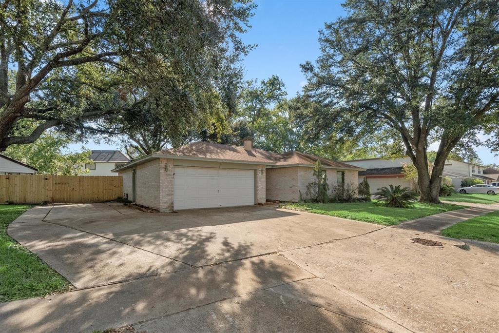 This single-story, suburban home features a two-car garage, a widened driveway, and a large tree providing shade in the front yard. The home has a well-maintained lawn and a privacy fence.