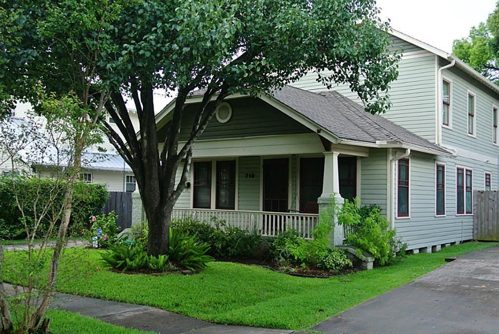 a view of brick house with a large windows plants and a large tree