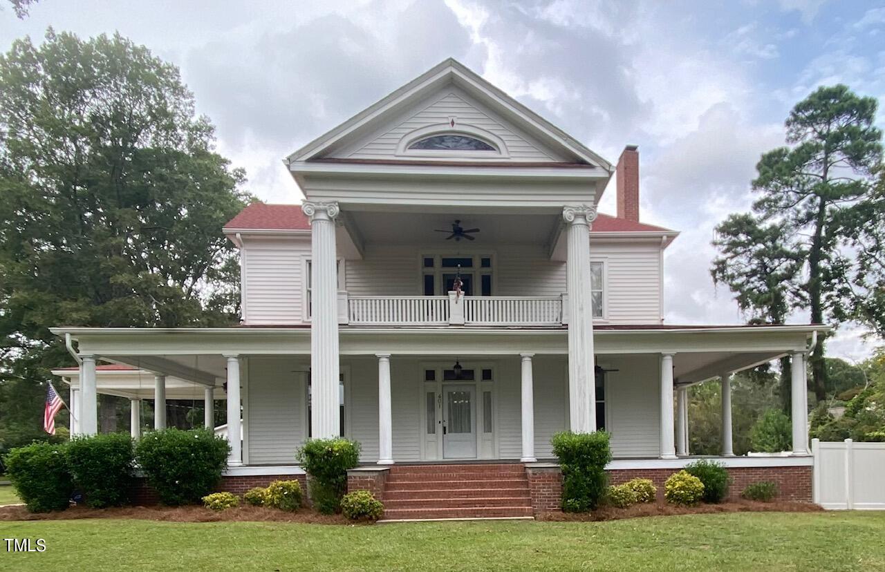 a view of a white house with a large windows and a yard with plants and large tree