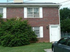 a brick house with a yard plants and large tree