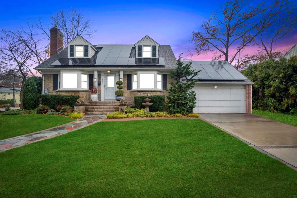 New england style home with solar panels, a garage, and a yard