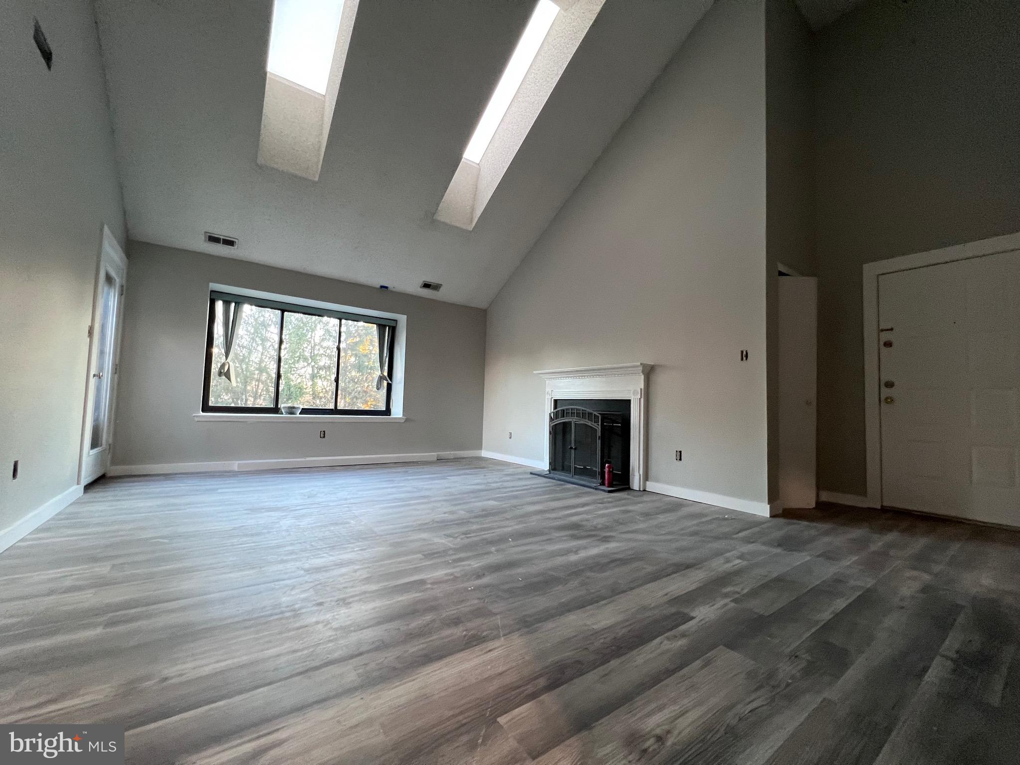 an empty room with wooden floor fireplace and windows