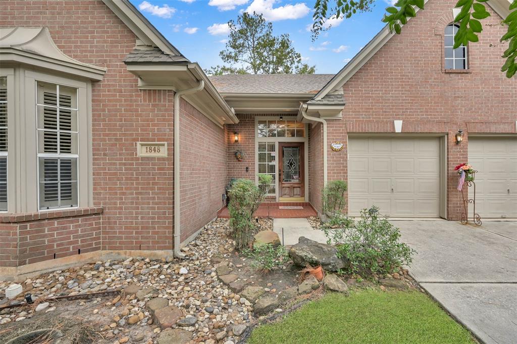 This is a single-story brick home featuring a two-car garage, a welcoming entryway with a decorative glass front door, and a well-maintained front yard with landscaping.