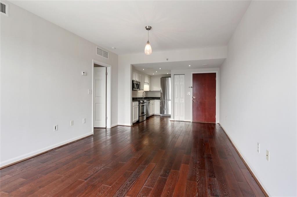 a view of empty room with wooden floor and kitchen