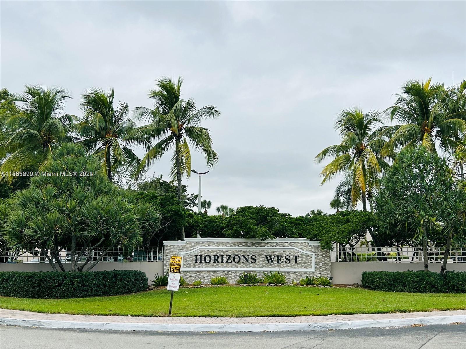 a view of green field with sign board and tall trees