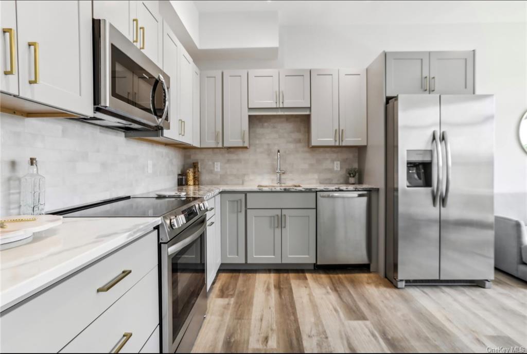 Kitchen featuring light stone counters, gray cabinets, appliances with stainless steel finishes, and light hardwood / wood-style floors