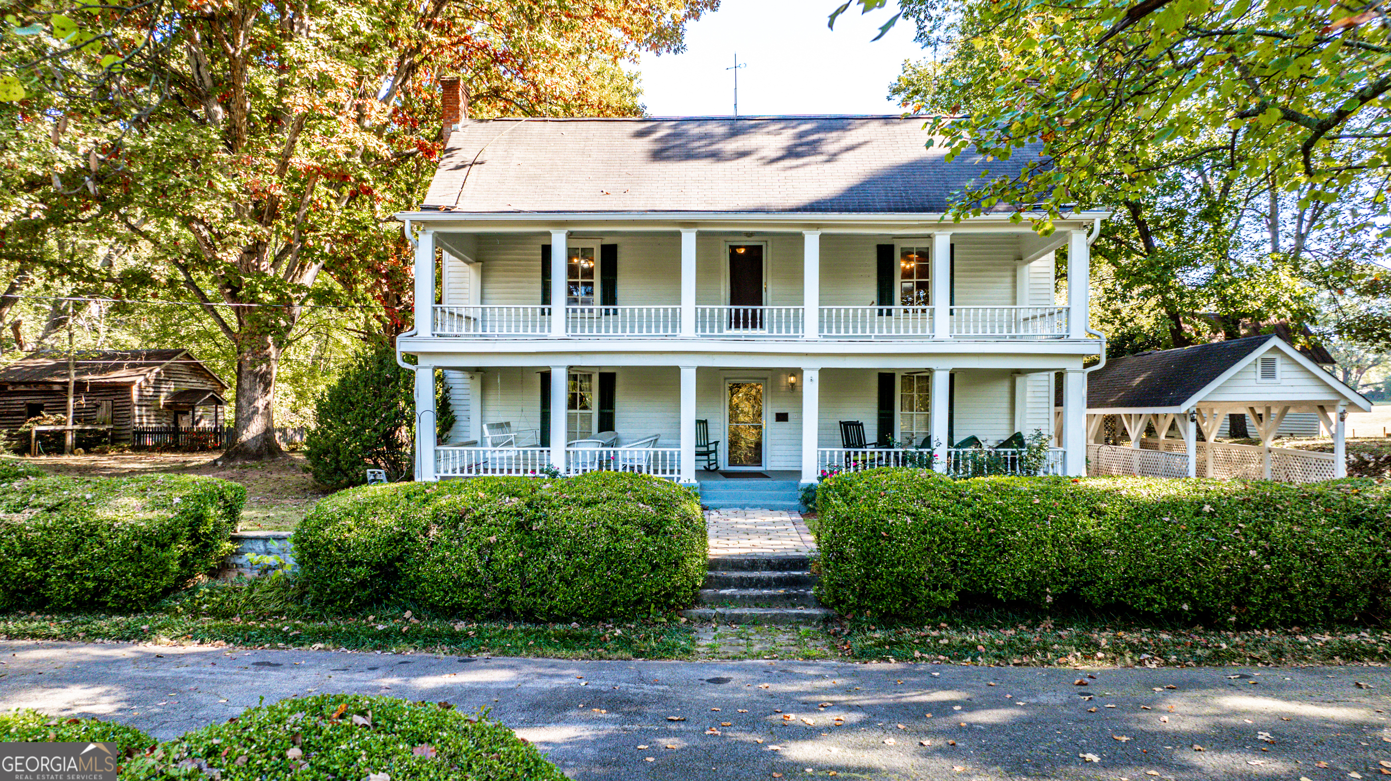 a view of a white house with large windows and a yard with plants and large trees