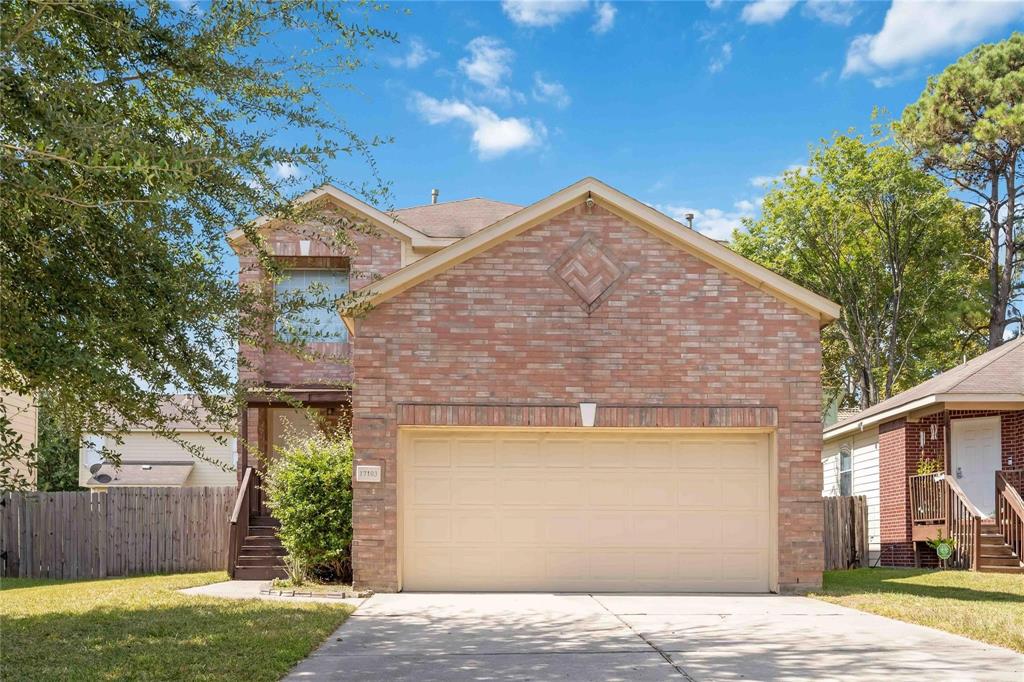 A charming two-story brick home with a well-maintained lawn and a two-car garage. The house features a classic design with a welcoming front porch.