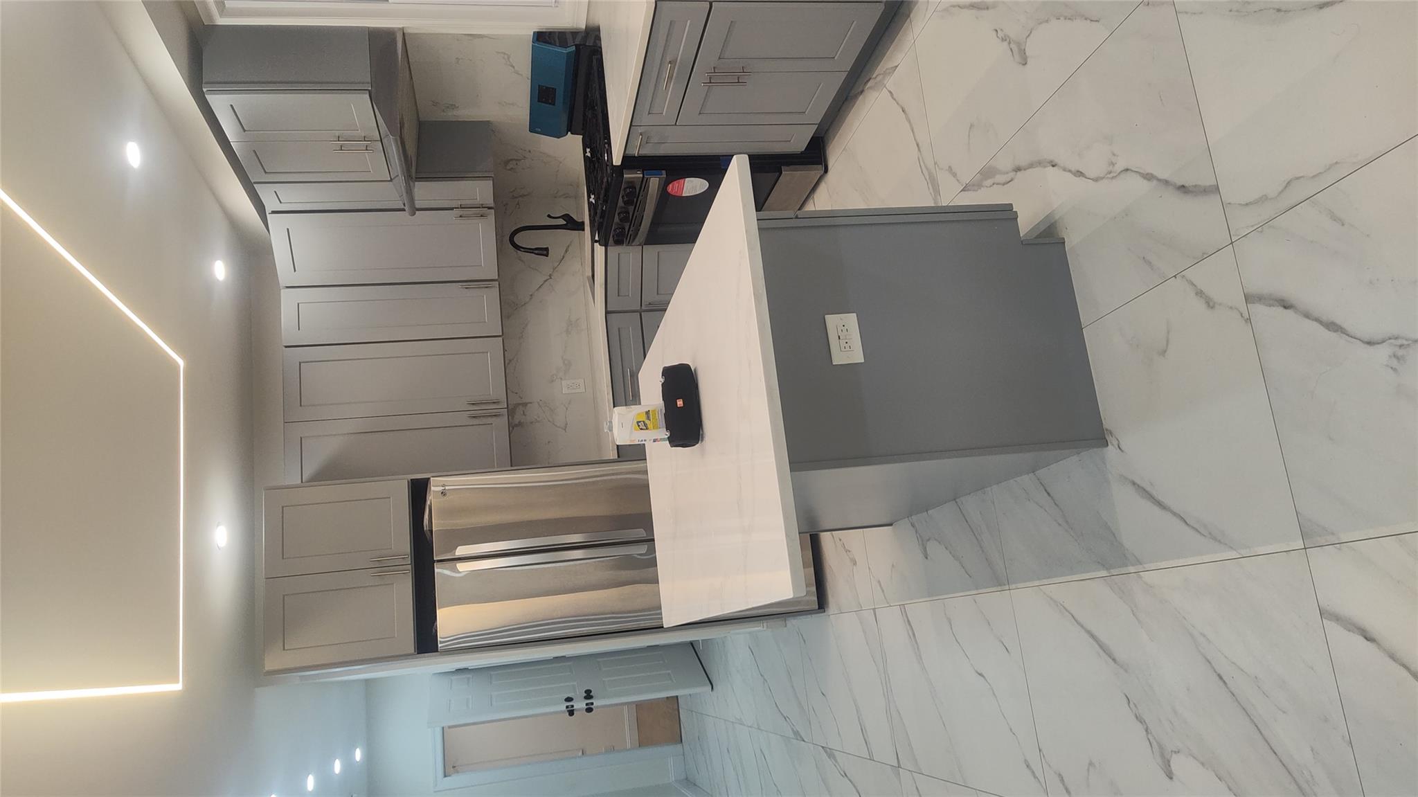 Kitchen featuring gray cabinetry, a center island, stove, refrigerator, and decorative backsplash