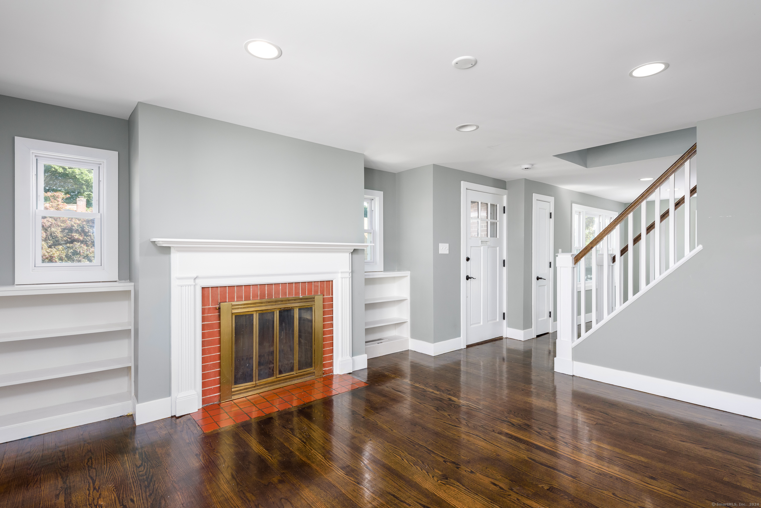 a view of an empty room with wooden floor fireplace and a window