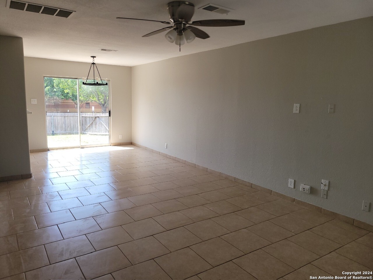 an empty room with chandelier fan and windows