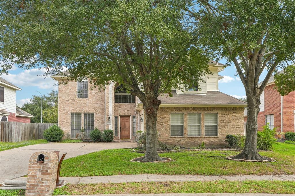 Two-story brick home with a welcoming front entrance. It features a well-maintained lawn, mature trees, and a driveway leading to a two-car garage.