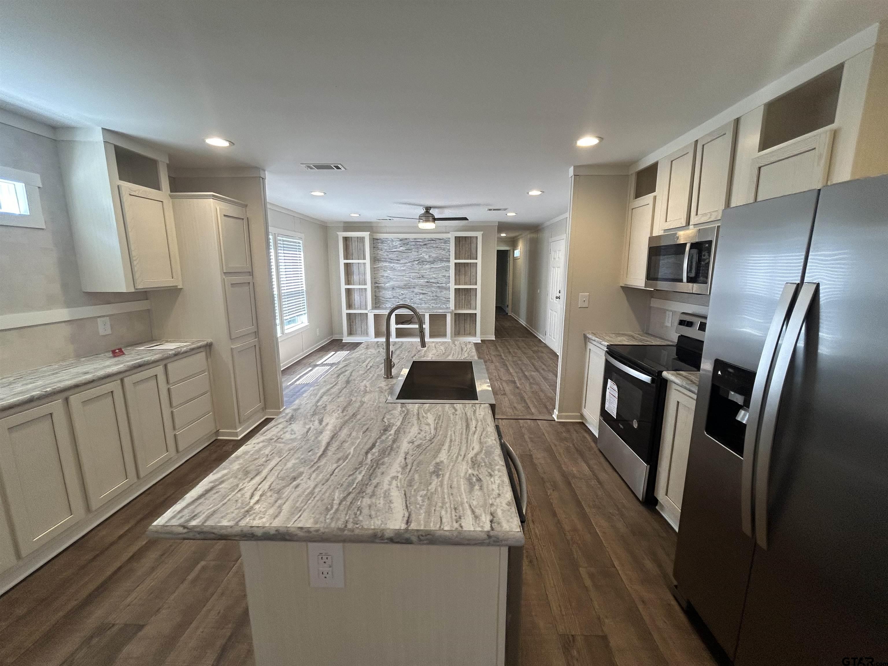 a kitchen with stainless steel appliances granite countertop a refrigerator a sink dishwasher and white cabinets next to a window