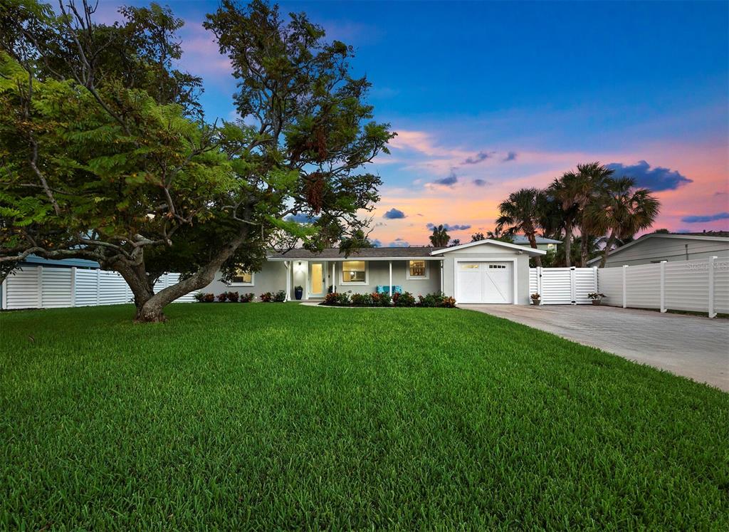 a view of a white house with a big yard plants and large trees