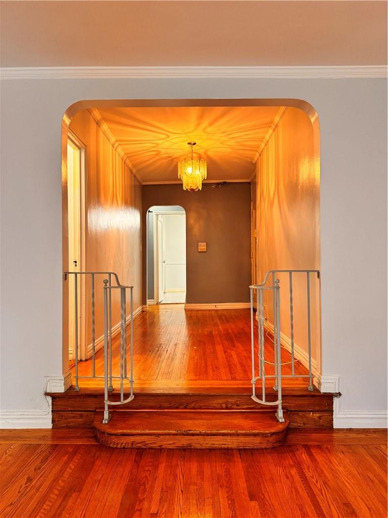 Stairs with an inviting chandelier, hardwood / wood-style floors, and ornamental molding