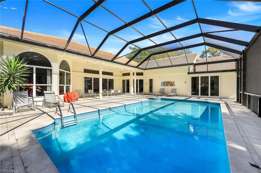 View of pool with glass enclosure, ceiling fan, and a patio area