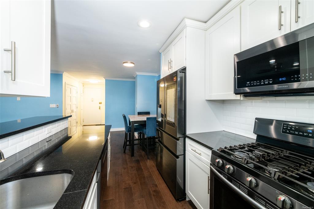 Kitchen featuring backsplash, sink, appliances with stainless steel finishes, dark hardwood / wood-style flooring, and white cabinetry