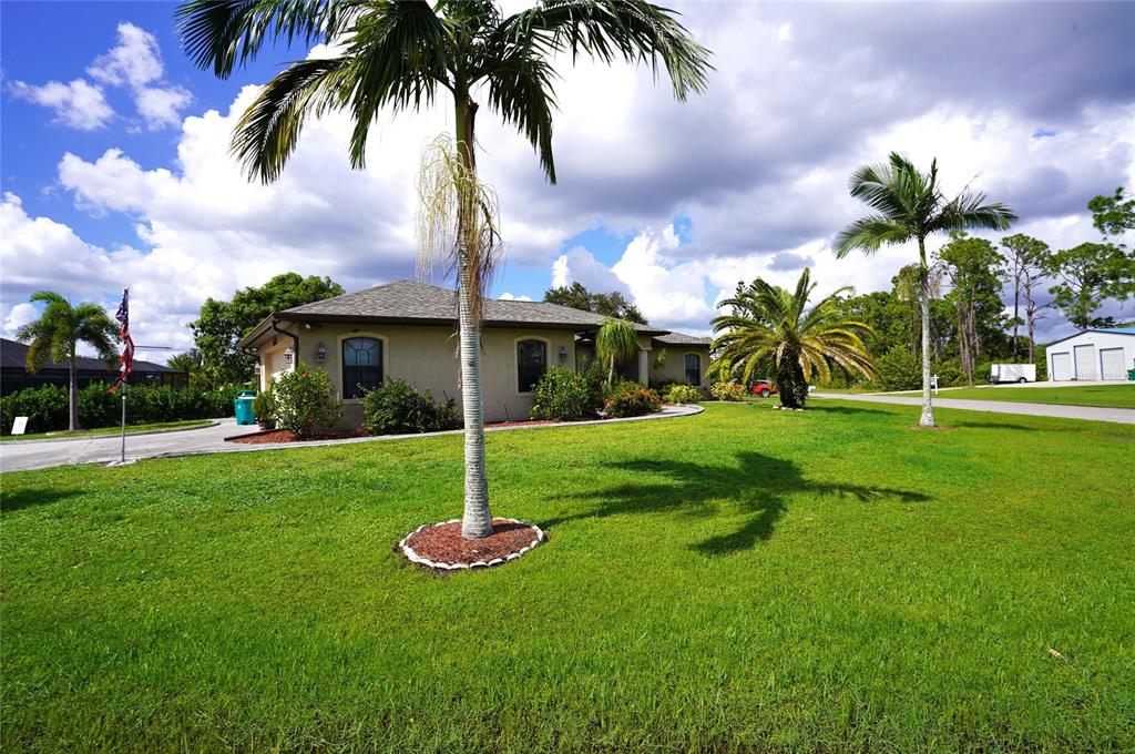 a front view of yellow house with a garden and palm trees