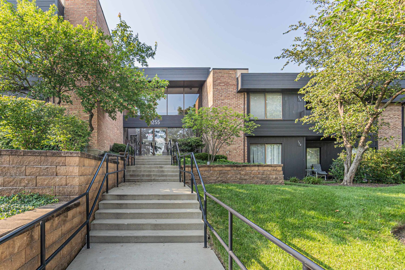 a view of a house with brick walls and a yard with plants and a large tree