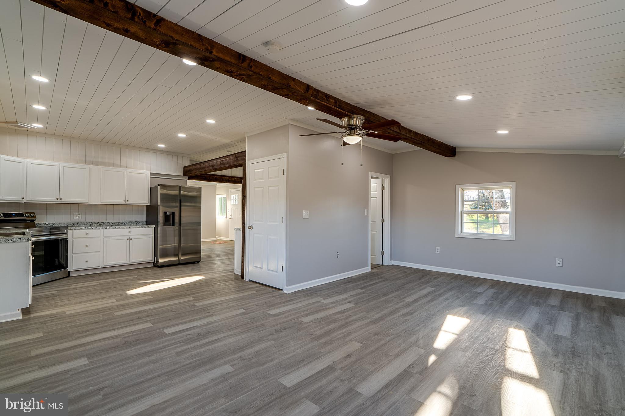 a view of an empty room with wooden floor and a kitchen