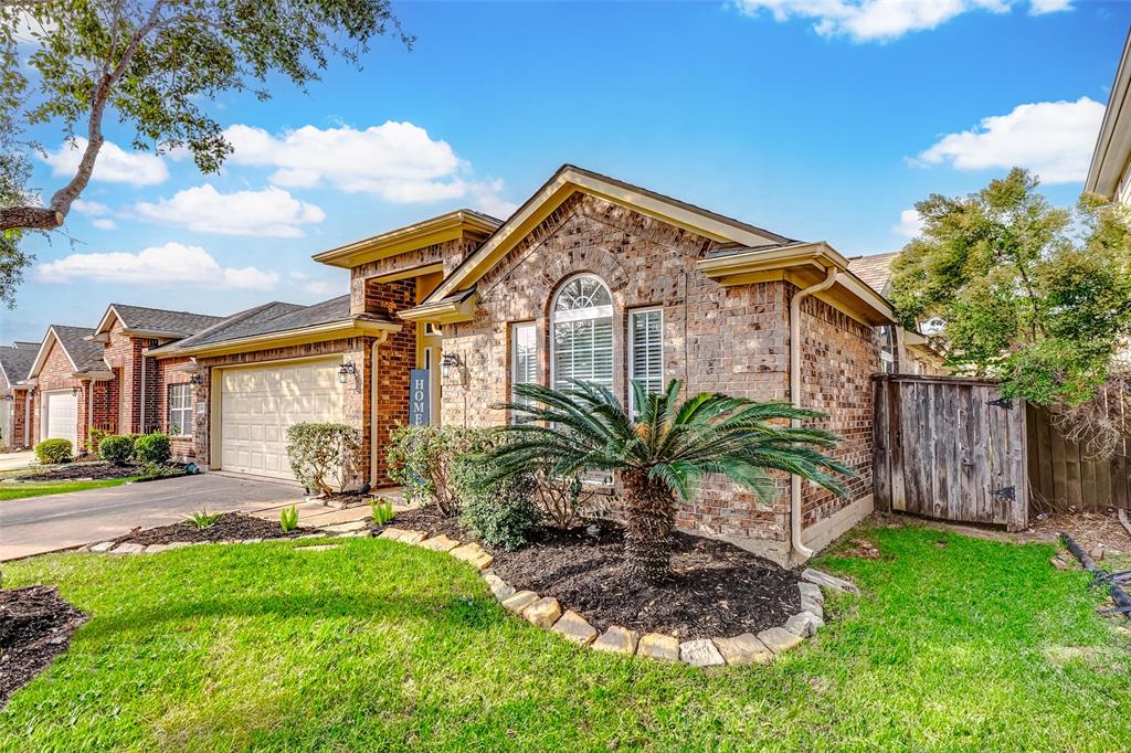 This stunning brick-front home boasts a welcoming front door, lush landscaping, and a spacious driveway leading to a 2-car attached garage. Meticulously maintained landscaping frames the front of the home, showcasing well-kept bushes, palm trees, and a vibrant lawn.