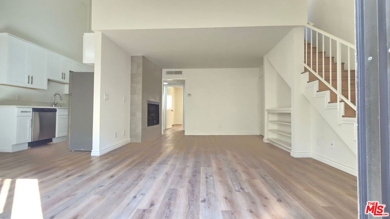 a view of empty room with wooden floor and kitchen