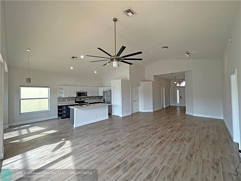 a view of a kitchen with kitchen island a sink wooden floor and stainless steel appliances