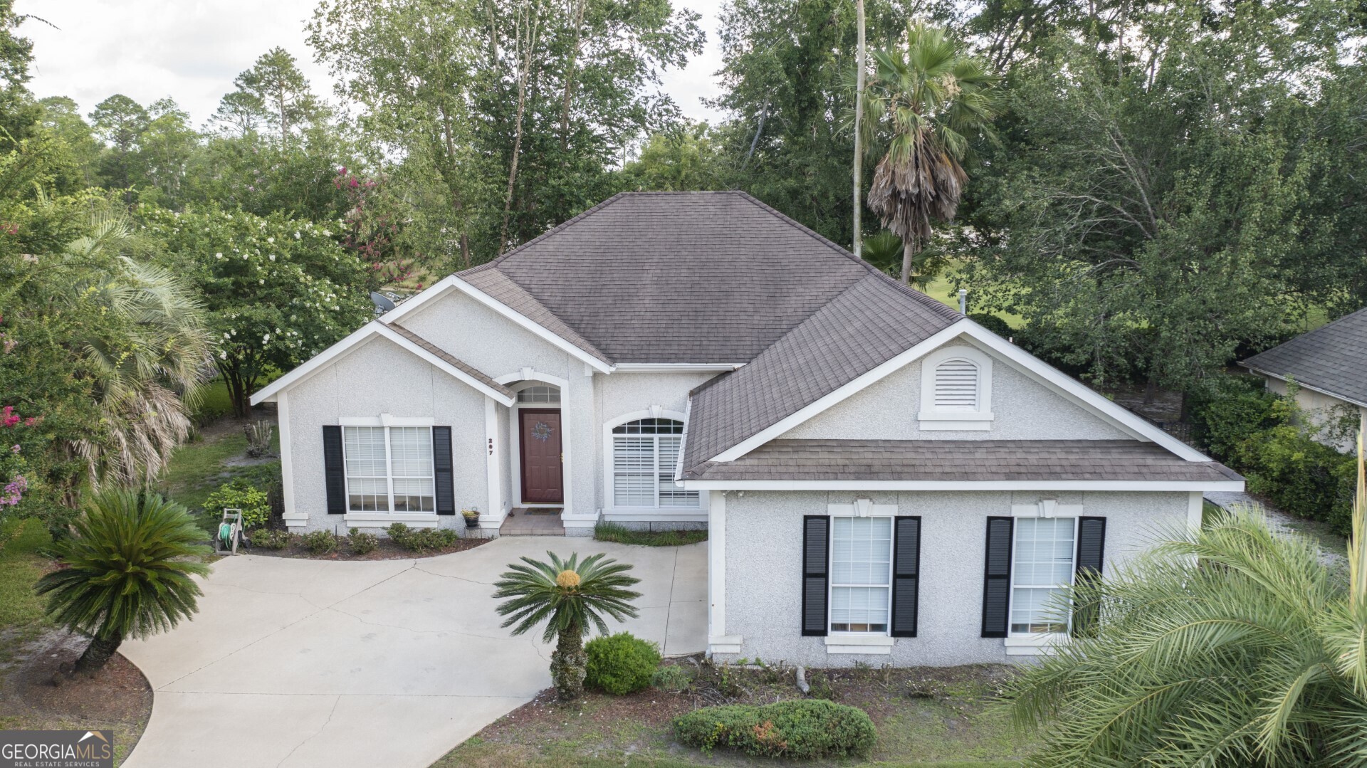 a view of a house with a yard plants and large tree