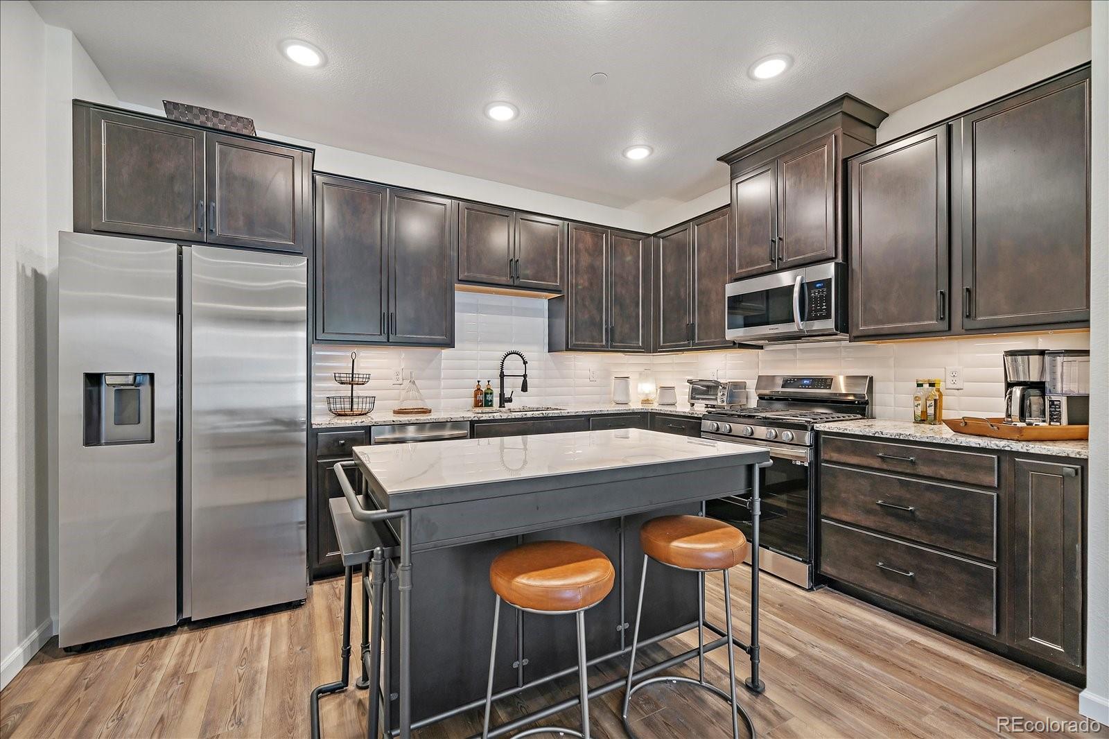 a kitchen with stainless steel appliances granite countertop a stove a sink a refrigerator and chairs with wooden floor
