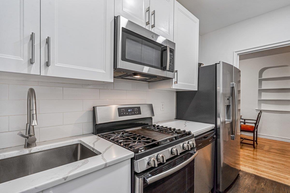 Kitchen featuring stainless steel appliances, white cabinetry, dark wood-type flooring, and sink