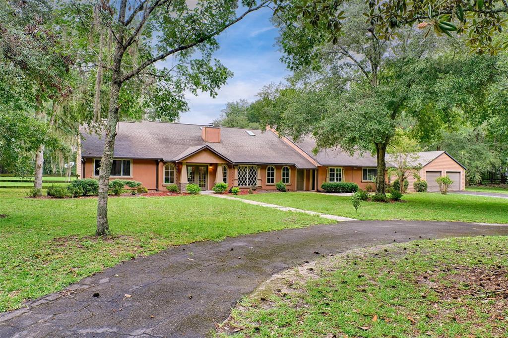 a view of house in front of a big yard with large trees