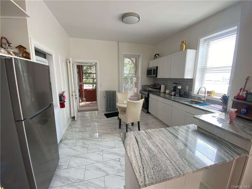 Kitchen featuring light stone countertops, stainless steel appliances, white cabinetry, and sink