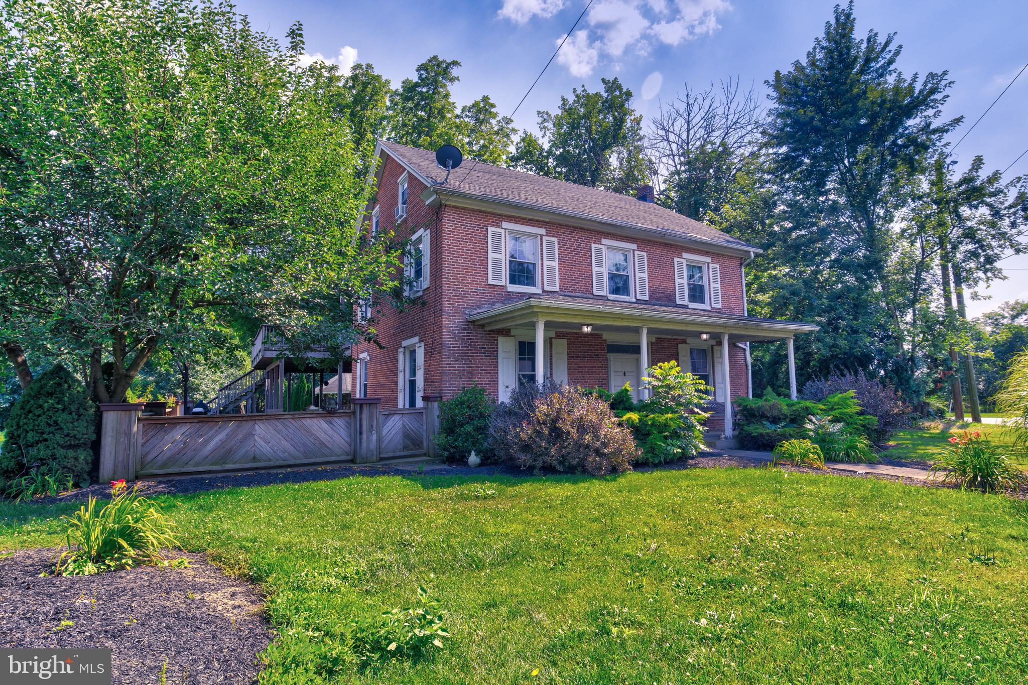 a view of a brick house with a yard plants and large tree