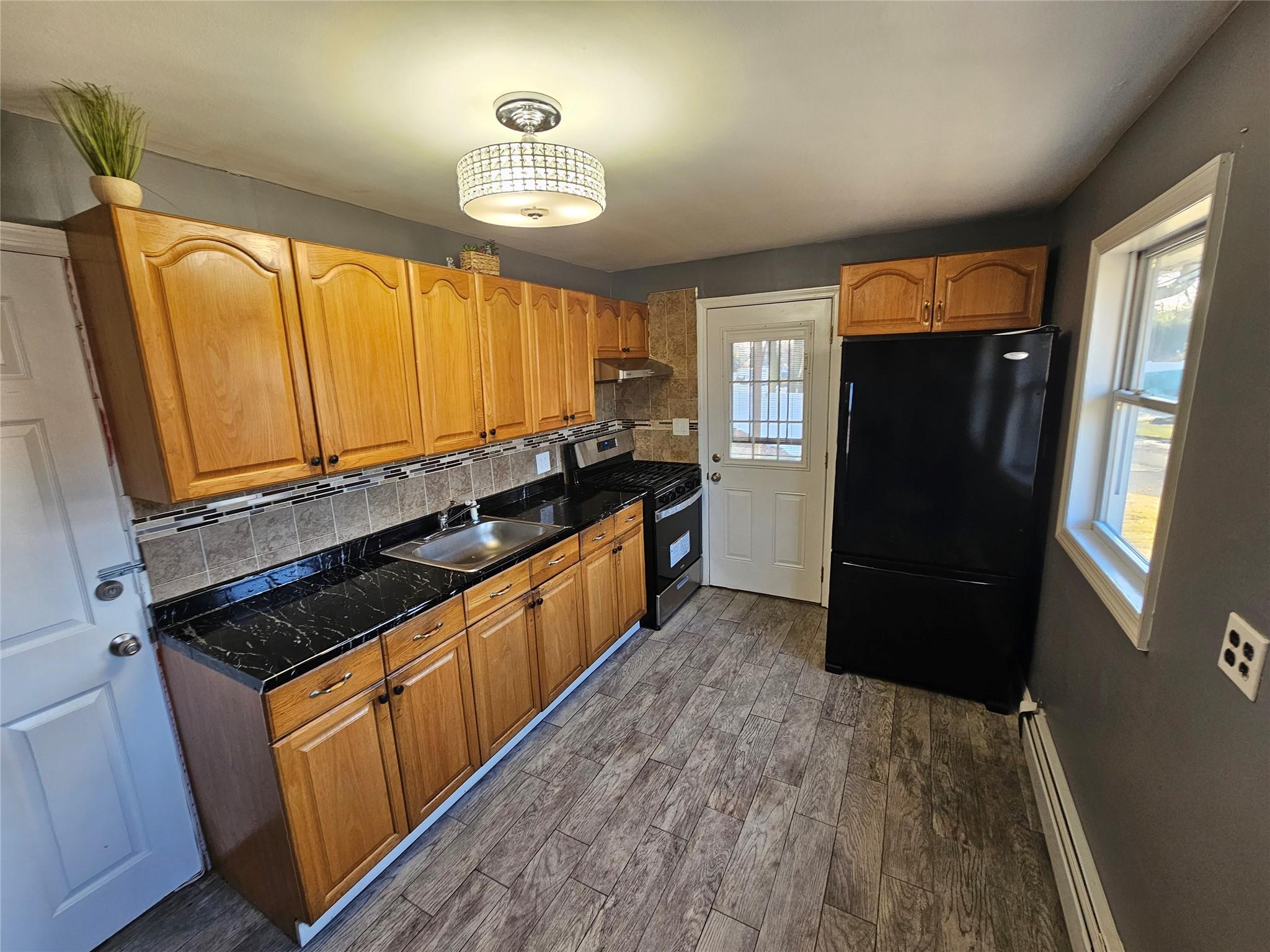 Kitchen featuring decorative backsplash, black fridge, a baseboard heating unit, sink, and stainless steel range oven