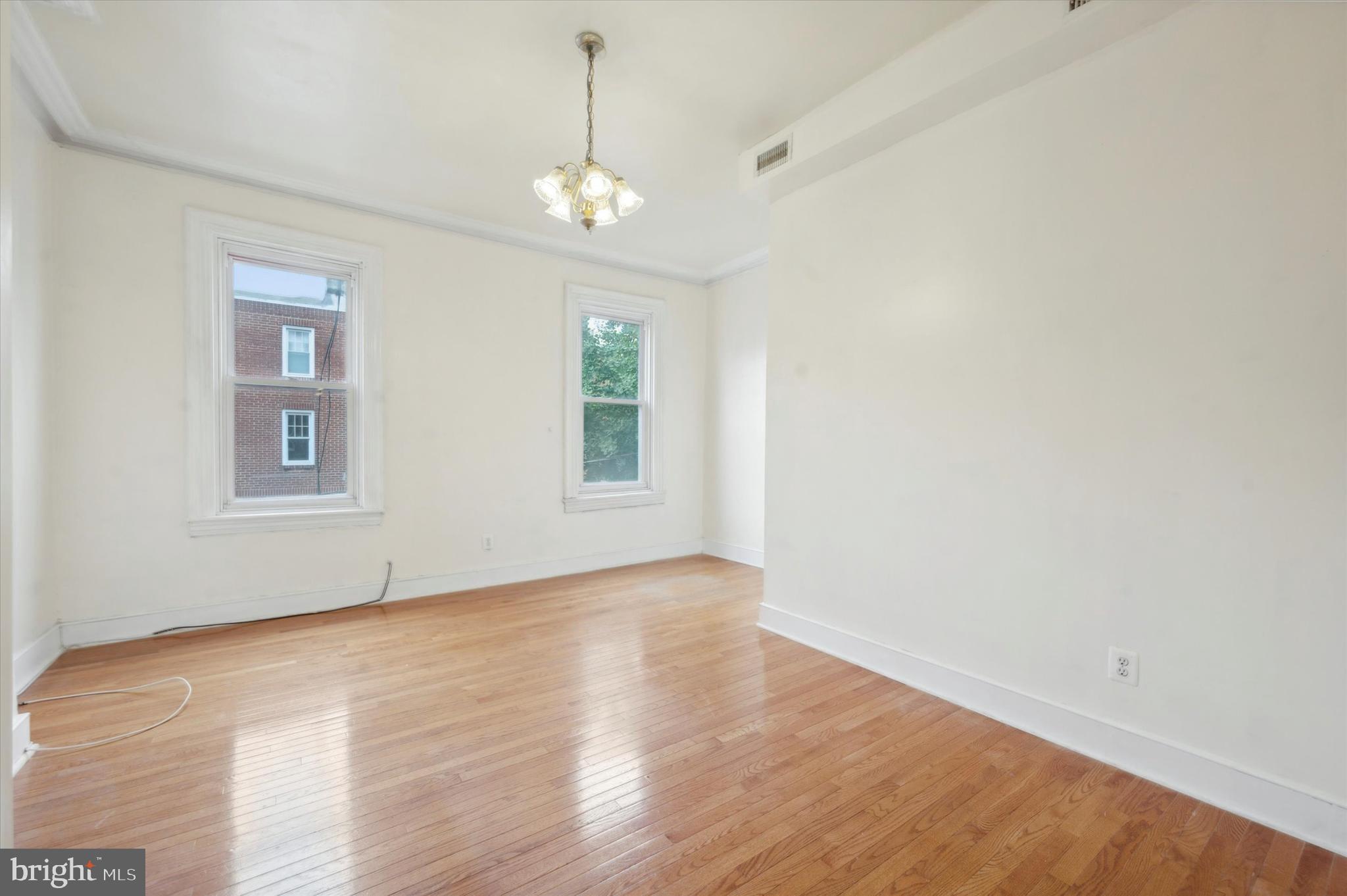 an empty room with wooden floor chandelier and windows