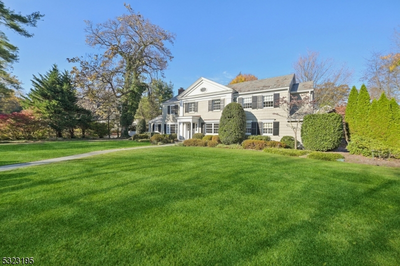 a view of a white house that has a big yard with plants and large trees